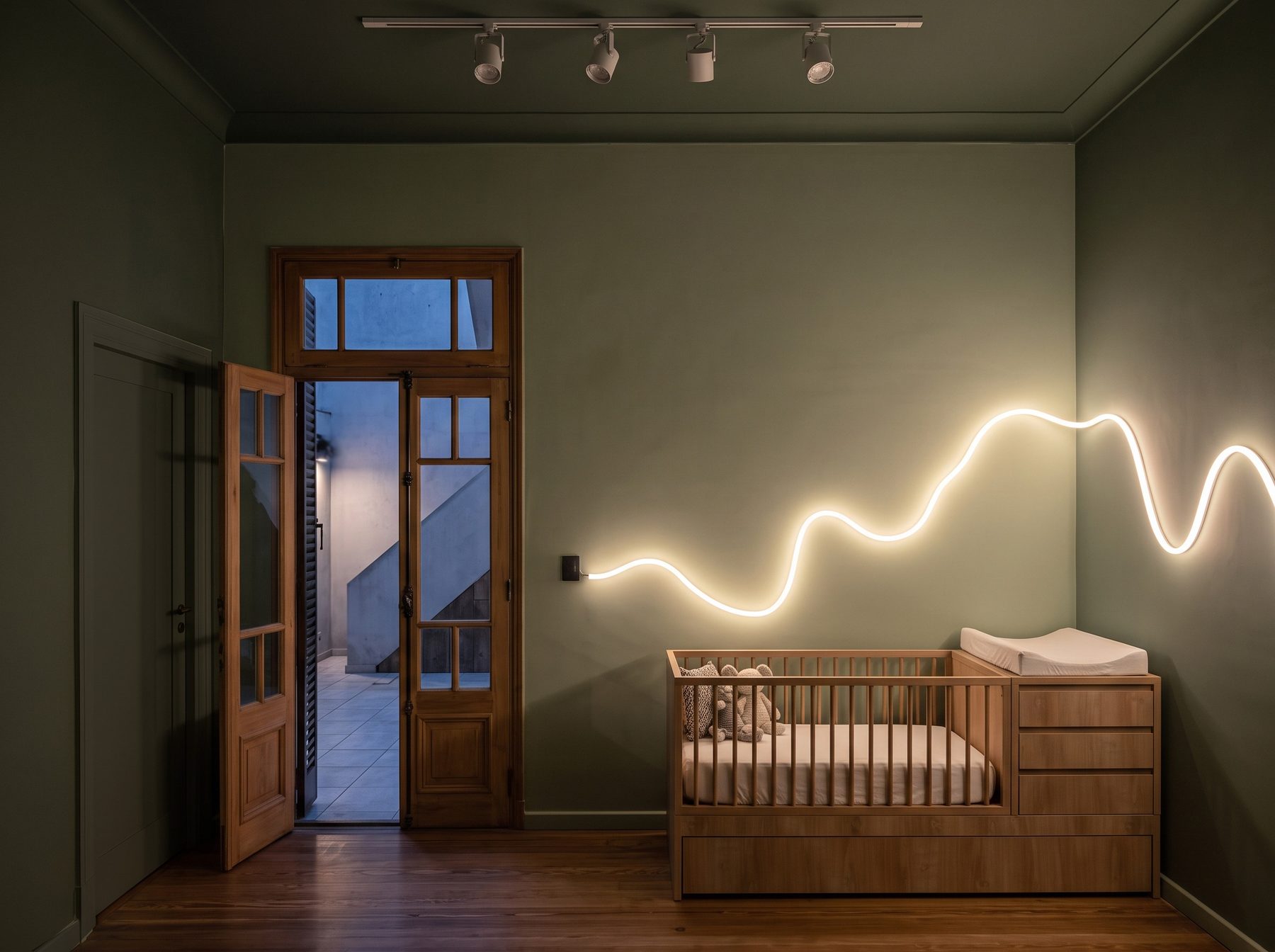 Propuesta: cuarto de bebé pintado en verde Dumbo, con cuna de madera, línea de luz neón ondulada y puerta de madera al patio