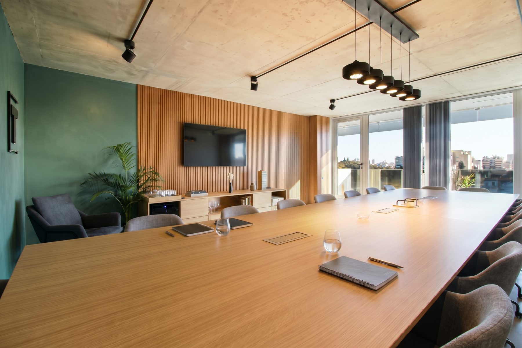 Mesa de roble para 18 personas, revestimiento de listones con pantalla, mueble bajo y ventanales a la ciudad